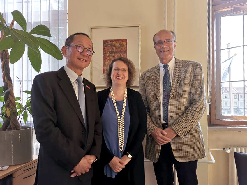 In einem Raum stehen von links nach rechts Professor Guo Hao, Professor Dr. Christina Strunck und Professor Dr. Günter Leugering und lächeln in die Kamera. 