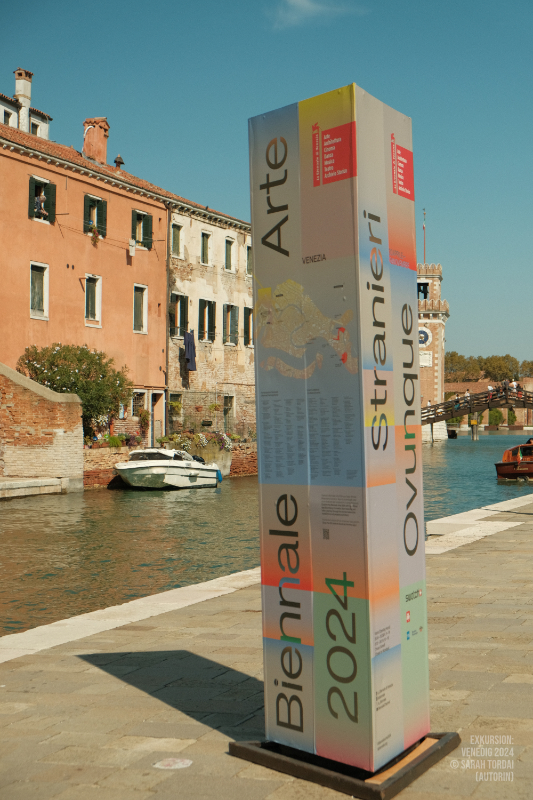 Informationssäule zur Biennale 2024 vor einem Kanal in Venedig
