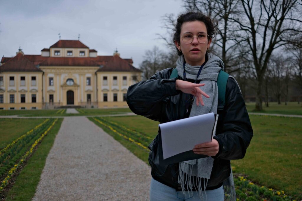 Junge Frau trägt Referat vor der Fassade des Schlosses Lustheim vor