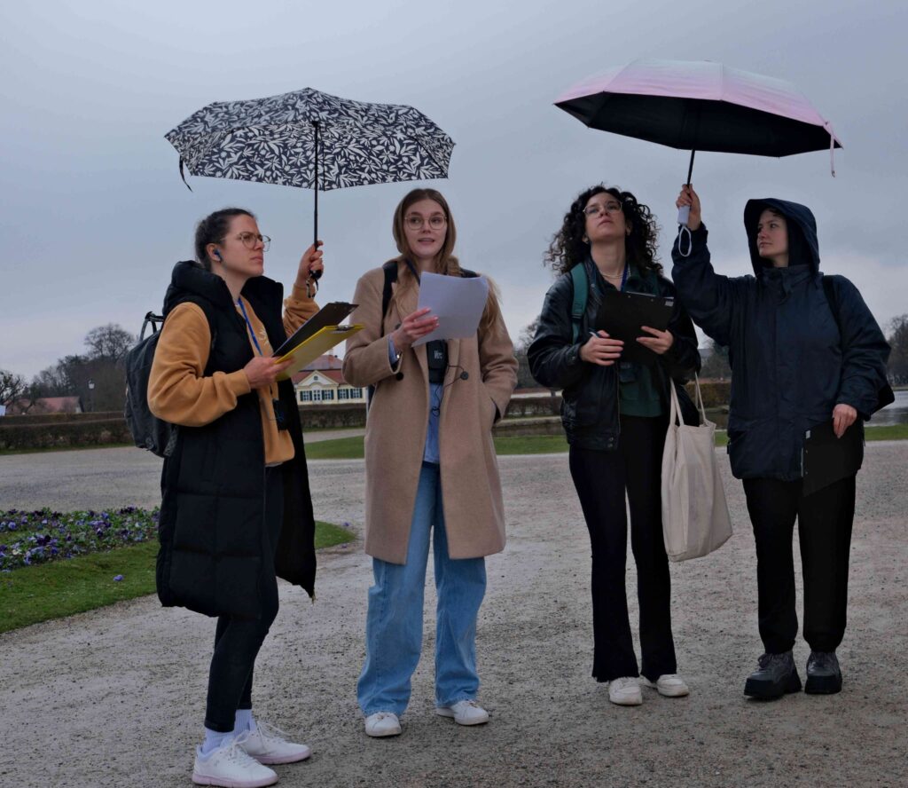Vier junge Frauen unter Regenschirmen in Vortragssituation